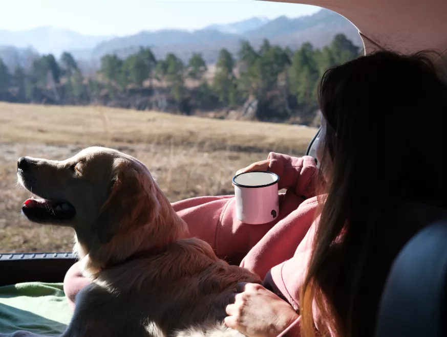 Eine Frau mit ihrem Goldenretriever genießt ihren Morgenkaffee, beim Camping mit Hund.jpg